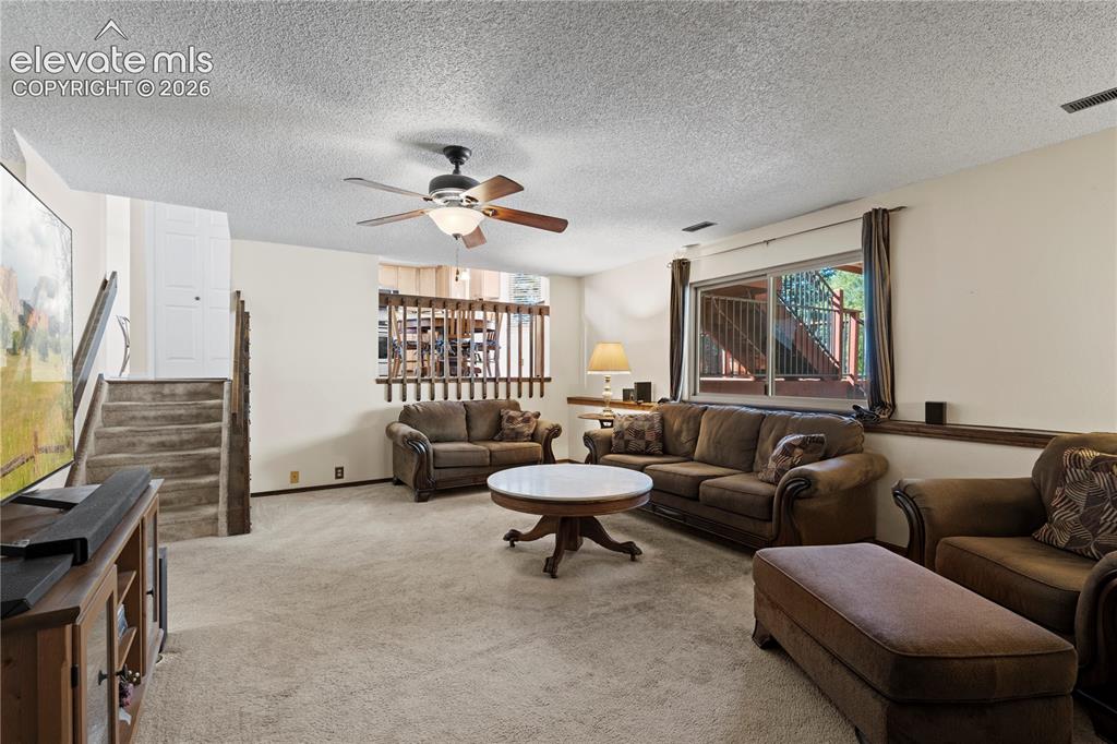 Image 22 of 43: Carpeted living area featuring a ceiling fan, a prominent window, and a woo