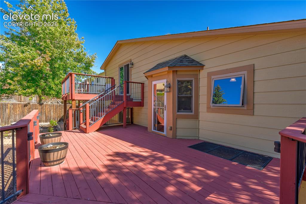 Image 27 of 43: Multi-level wood deck with black metal railings and a bay window feature