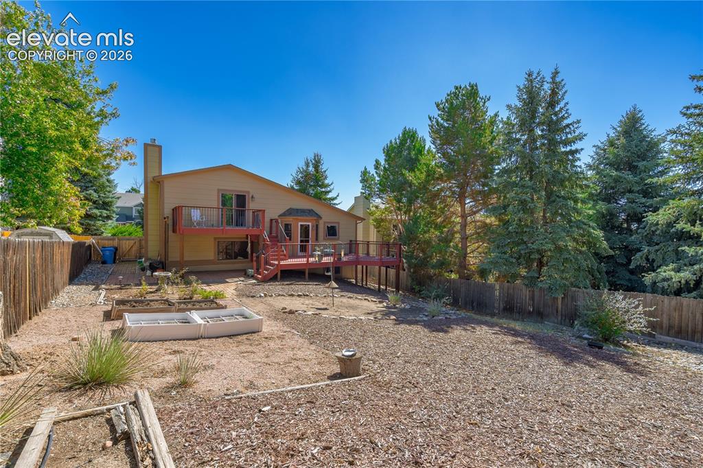 Image 29 of 43: Fenced backyard with multi-level wood deck, established trees, and raised p