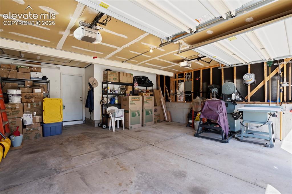 Image 36 of 43: Concrete flooring with exposed ceiling joists and two overhead garage door 