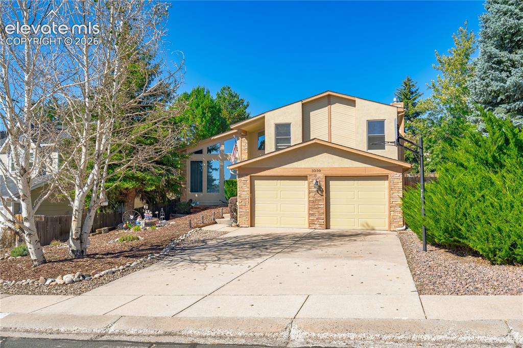 Image 39 of 43: Two-car garage, stone facade accents, large driveway, mature landscaping, a