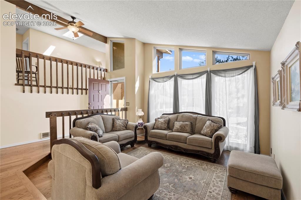 Image 5 of 43: Expansive living area with vaulted ceilings, wood-finish flooring, and a ce