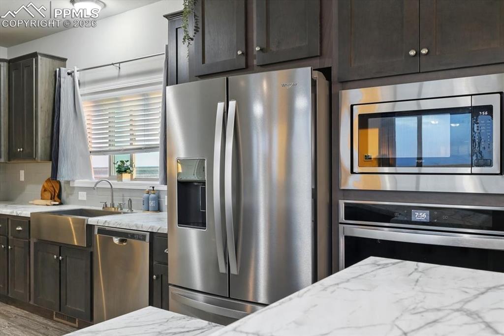 Image 13 of 30: Kitchen featuring stainless steel appliances, a sink, light stone counterto