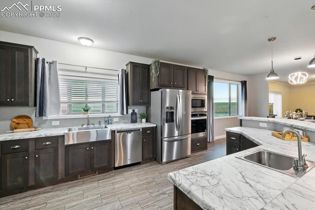 Image 14 of 30: Kitchen with stainless steel appliances, a sink, pendant lighting, and wood