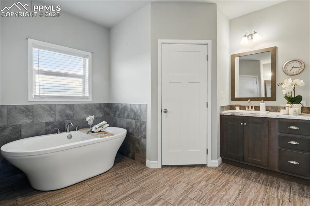 Image 17 of 30: Full bath with tile walls, a soaking tub, vanity, a wainscoted wall, and wo
