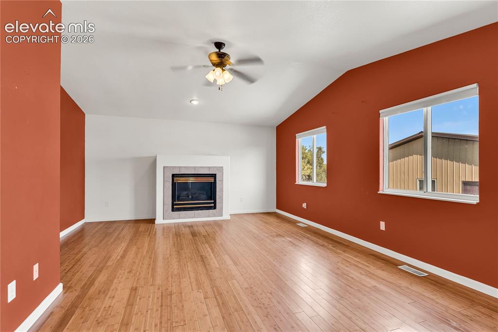 Image 11 of 32: Vaulted ceiling featuring a ceiling fan, wood-finish flooring, and a firepl