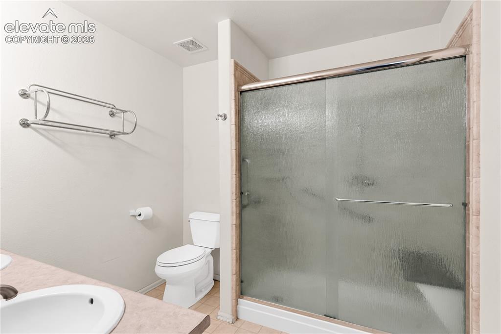 Image 16 of 32: Sliding glass shower enclosure with tiled surround, white toilet, and count