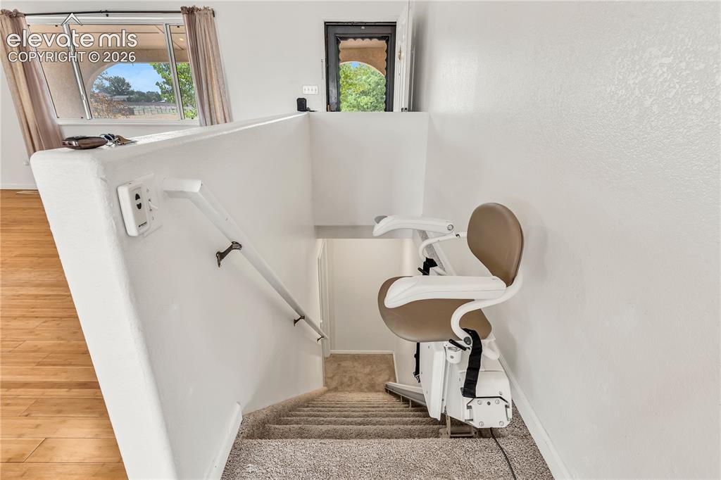 Image 18 of 32: Carpeted staircase with an installed stair lift system, featuring a handrai