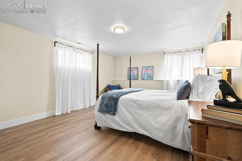 Image 15 of 45: Bedroom with wallpapered walls and wood finished floors