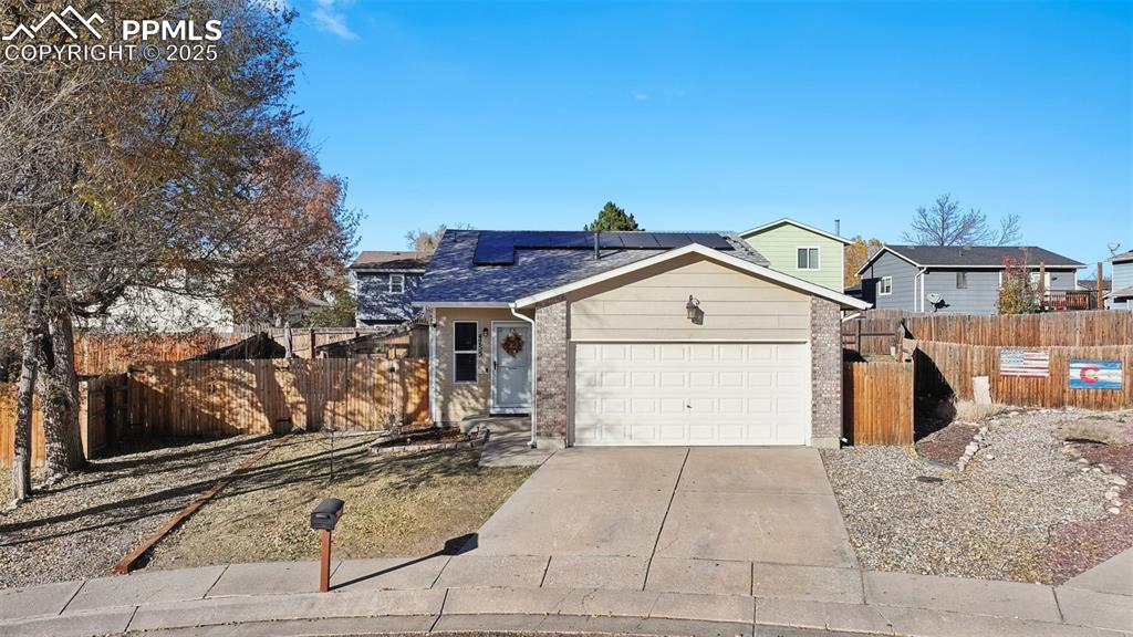 Caption: View of front facade with roof mounted solar panels, brick siding, driveway, a garage, and a shingle