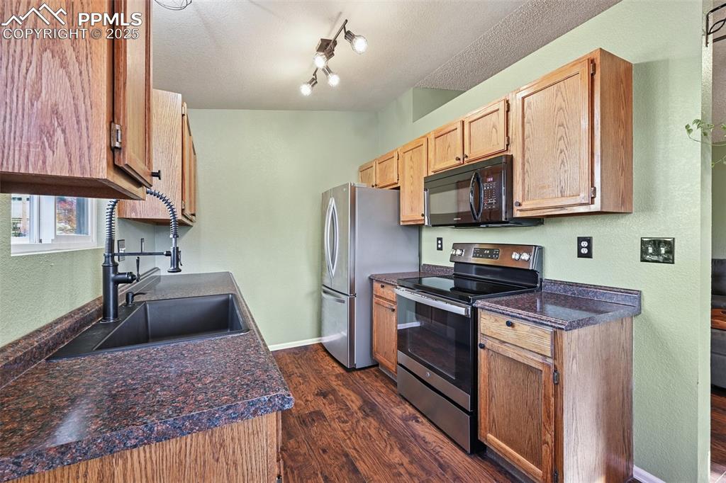 Image 13 of 23: Kitchen with dark countertops, stainless steel electric range oven, dark wo