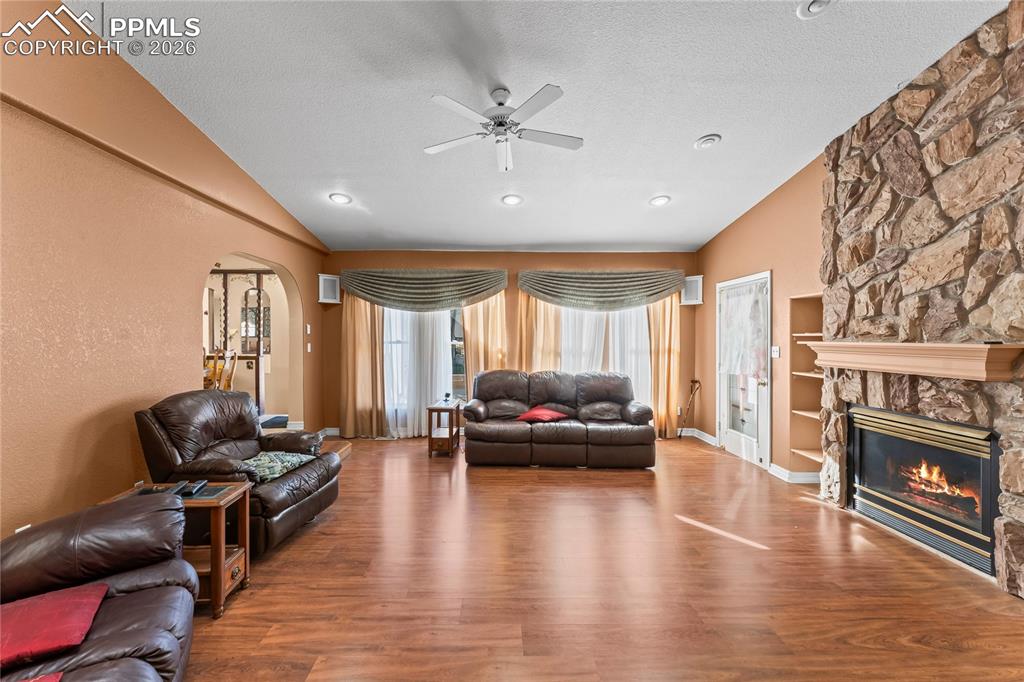 Image 15 of 41: Living area featuring arched walkways, ceiling fan, a fireplace, wood finis