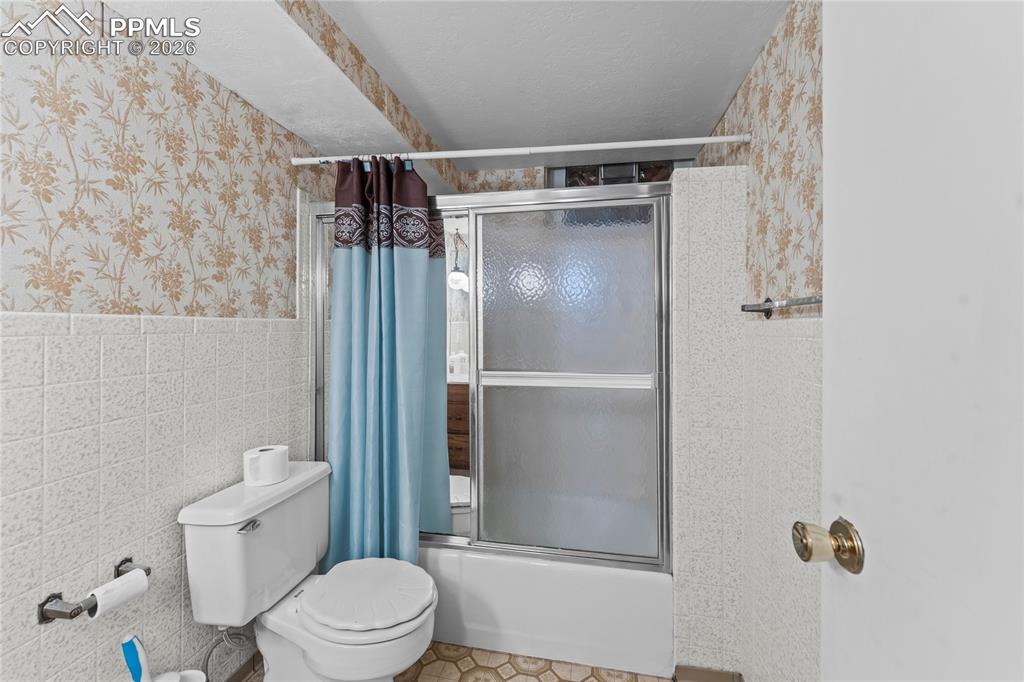 Image 34 of 41: Full bath featuring wallpapered walls, enclosed tub / shower combo, tile wa