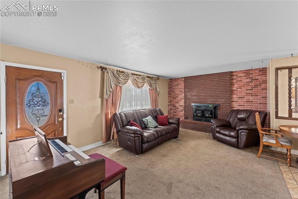 Image 5 of 41: Living room with light carpet, brick wall, a fireplace, and a textured ceil
