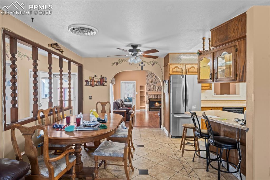 Image 8 of 41: Dining room with arched walkways, ceiling fan, a stone fireplace, light til