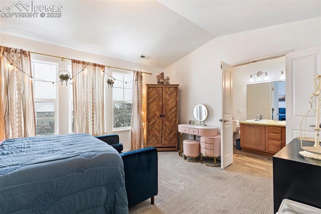 Image 26 of 34: Bedroom with vaulted ceiling, light carpet, a sink, and connected bathroom