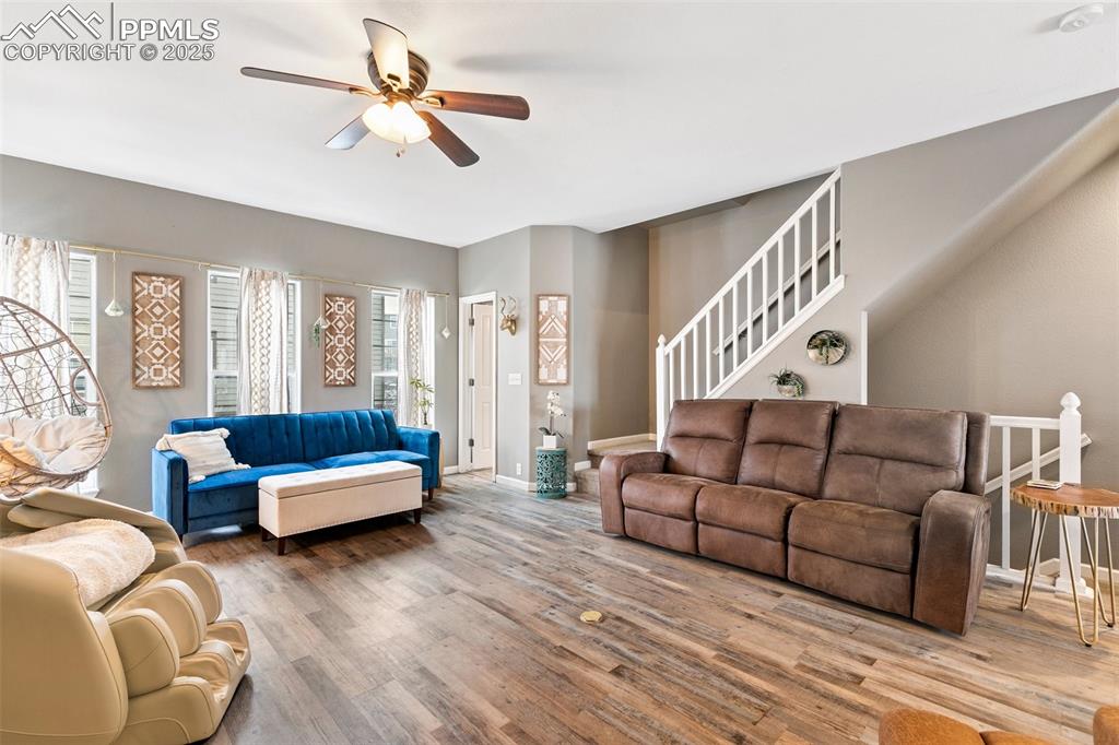 Image 6 of 34: Living room featuring a ceiling fan, wood finished floors, stairway, and ba