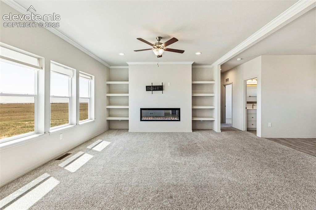 Image 11 of 38: Spacious living area featuring a built-in electric fireplace with mounted s