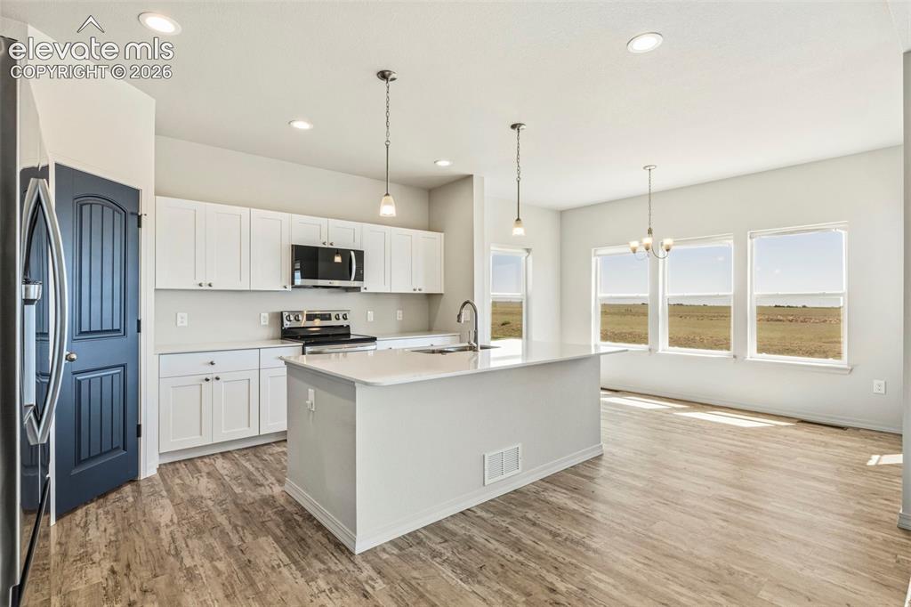 Image 12 of 38: Open-concept kitchen featuring white shaker cabinetry, an island with an un