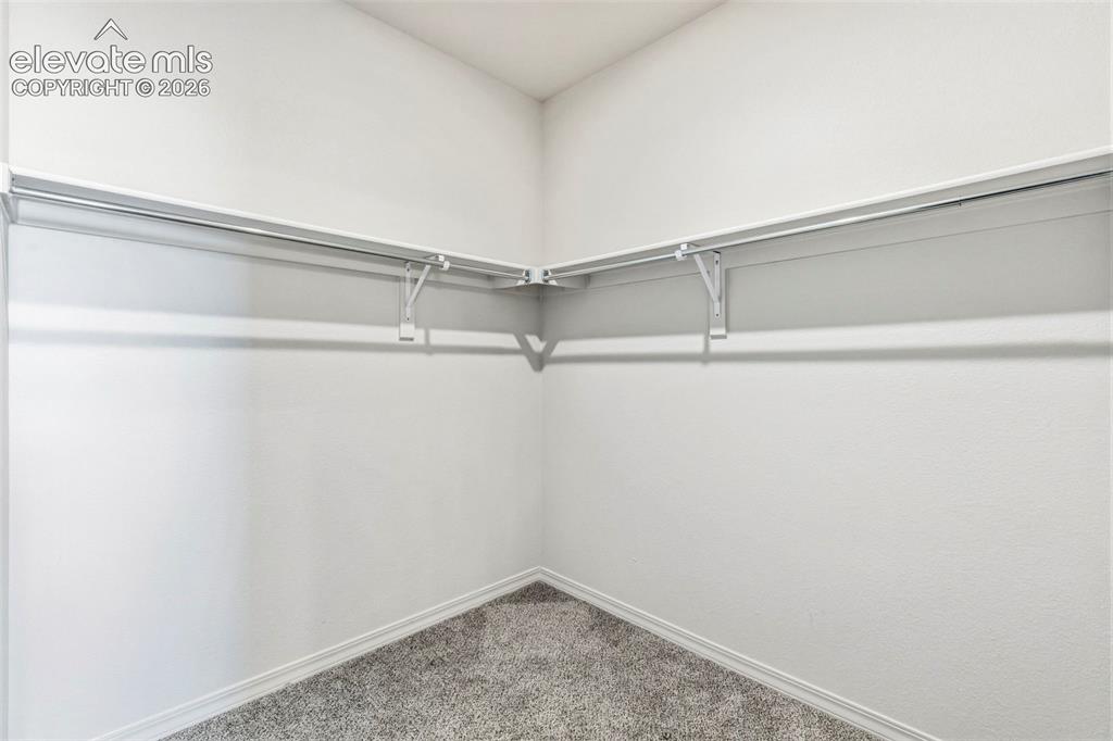 Image 25 of 38: Corner closet featuring white shelving and chrome hanging rods