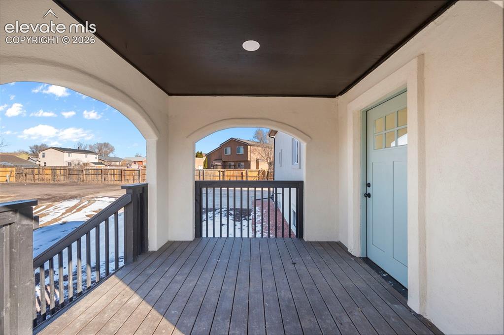 Image 13 of 50: Covered front porch with wood-finish decking, dark contrasting railings, an