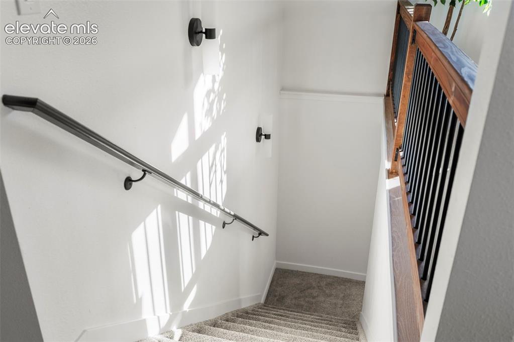Image 32 of 50: Stairwell featuring carpeted steps, a black metal handrail, white wall scon