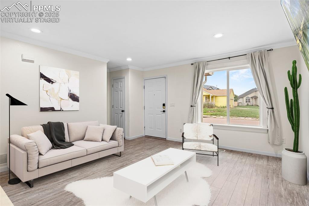 Image 10 of 39: Living room with crown molding, light wood finished floors, and recessed li
