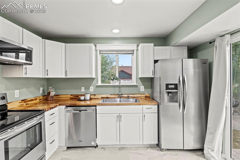 Image 13 of 39: Kitchen with wooden counters, appliances with stainless steel finishes, whi