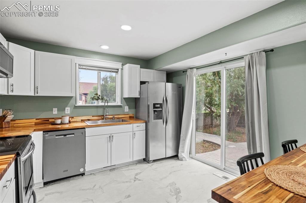 Image 15 of 39: Kitchen with wooden counters, light marble finish floors, appliances with s