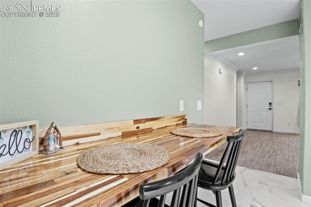 Image 18 of 39: Dining area with ornamental molding, marble look tile flooring, and recesse