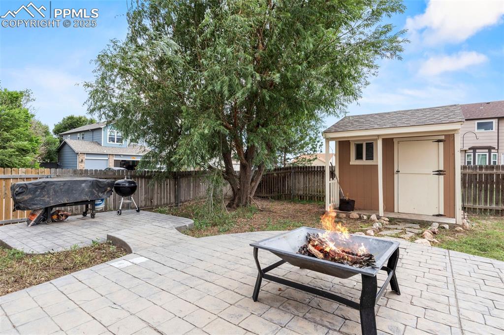 Image 35 of 39: Fenced backyard with an outdoor fire pit, a storage shed, a patio area, and