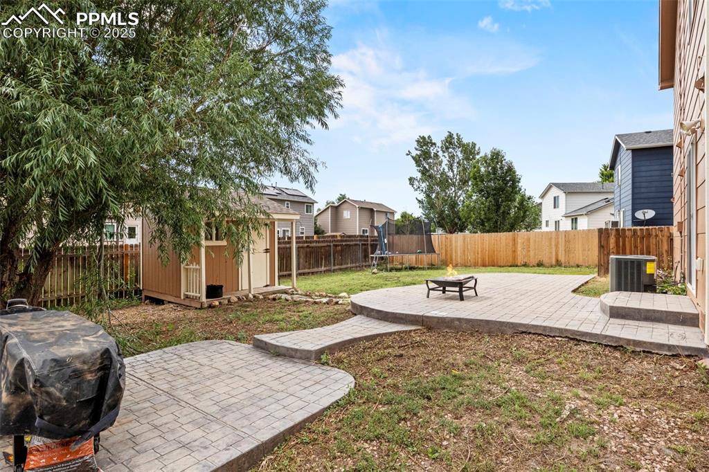 Image 36 of 39: Fenced backyard featuring a shed, a trampoline, a patio area, a fire pit, a