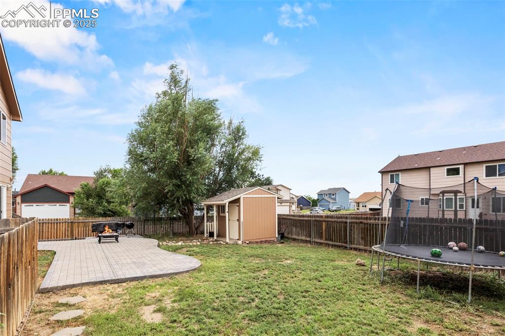 Image 37 of 39: Fenced backyard featuring a trampoline, a patio area, a shed, and a residen