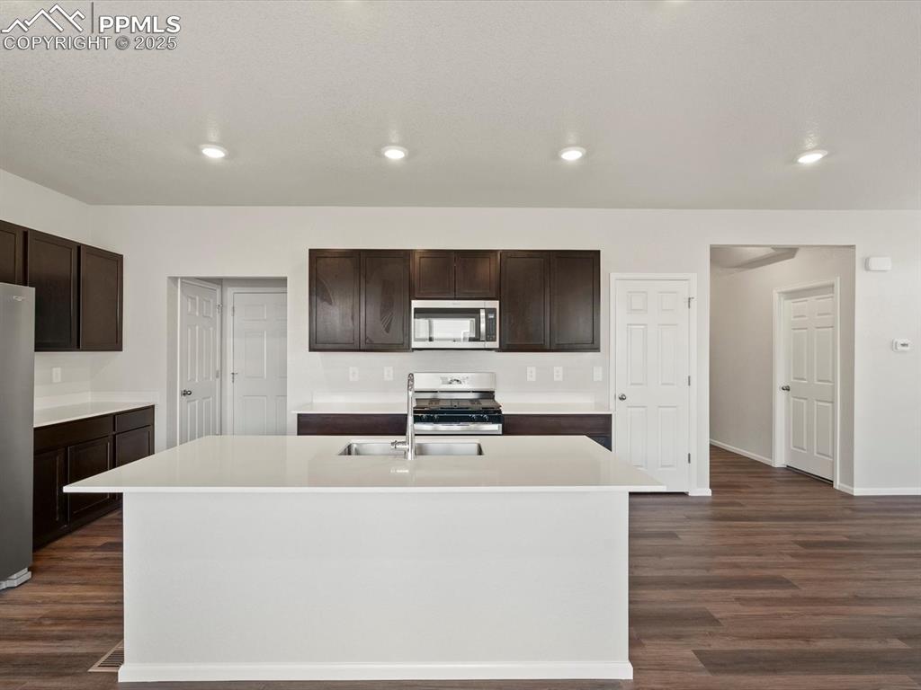 Image 10 of 25: Kitchen with dark brown cabinetry, recessed lighting, appliances with stain