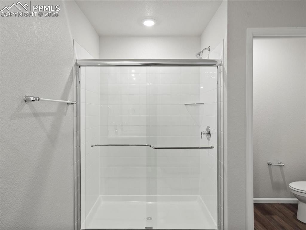 Image 17 of 25: Bathroom featuring a stall shower, a textured wall, and dark wood finished