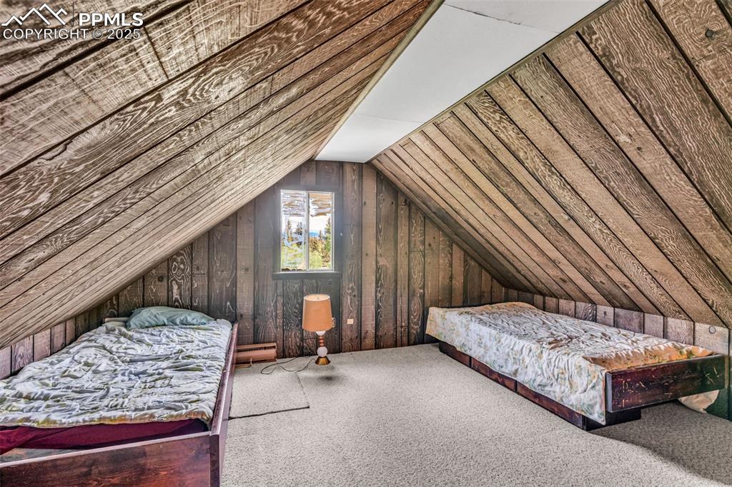 Image 14 of 33: Carpeted bedroom featuring wood walls, vaulted ceiling, and baseboard heati