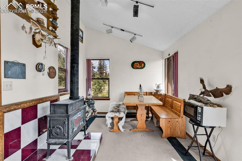 Image 21 of 33: Dining area featuring track lighting, a wood stove, vaulted ceiling, and ca