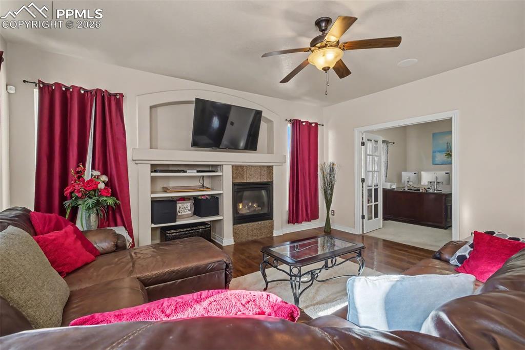 Image 22 of 49: Living room with gas fireplace with niche, ceiling fan and hardwood floors