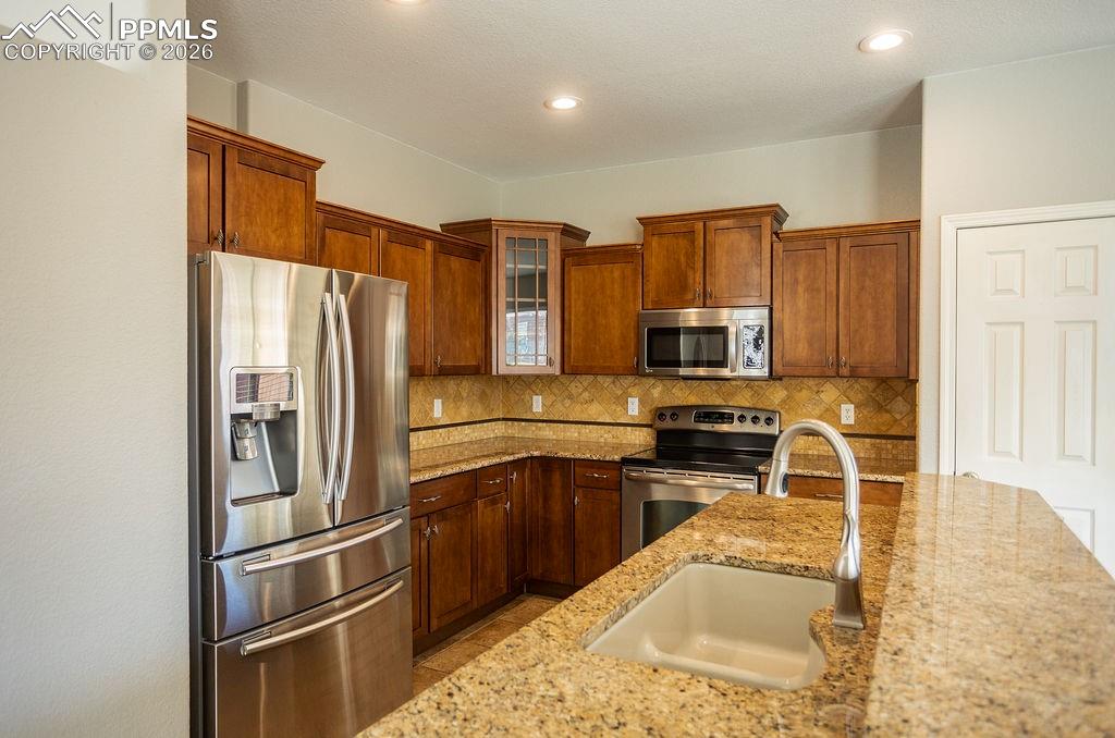 Image 11 of 49: Kitchen with stainless steel appliances, glass fronted cabinets, light ston