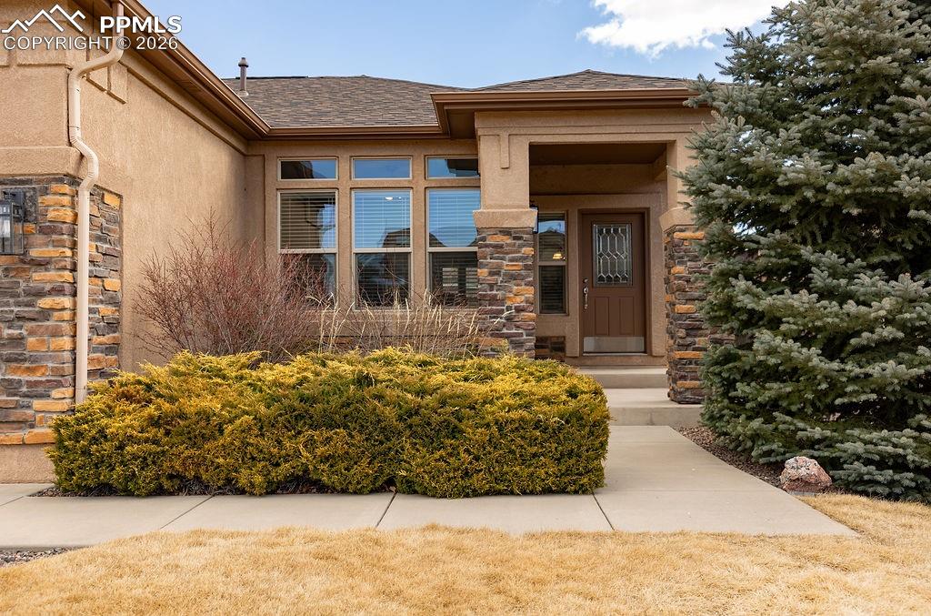 Image 2 of 49: Entrance to property with a shingled roof, stone siding, and stucco siding