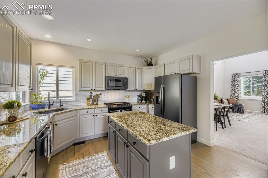 Image 12 of 32: Kitchen with gray cabinets, light stone countertops, black appliances, tast
