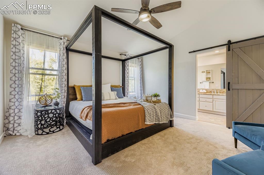 Image 19 of 32: Bedroom featuring a barn door, light colored carpet, a ceiling fan, ensuite