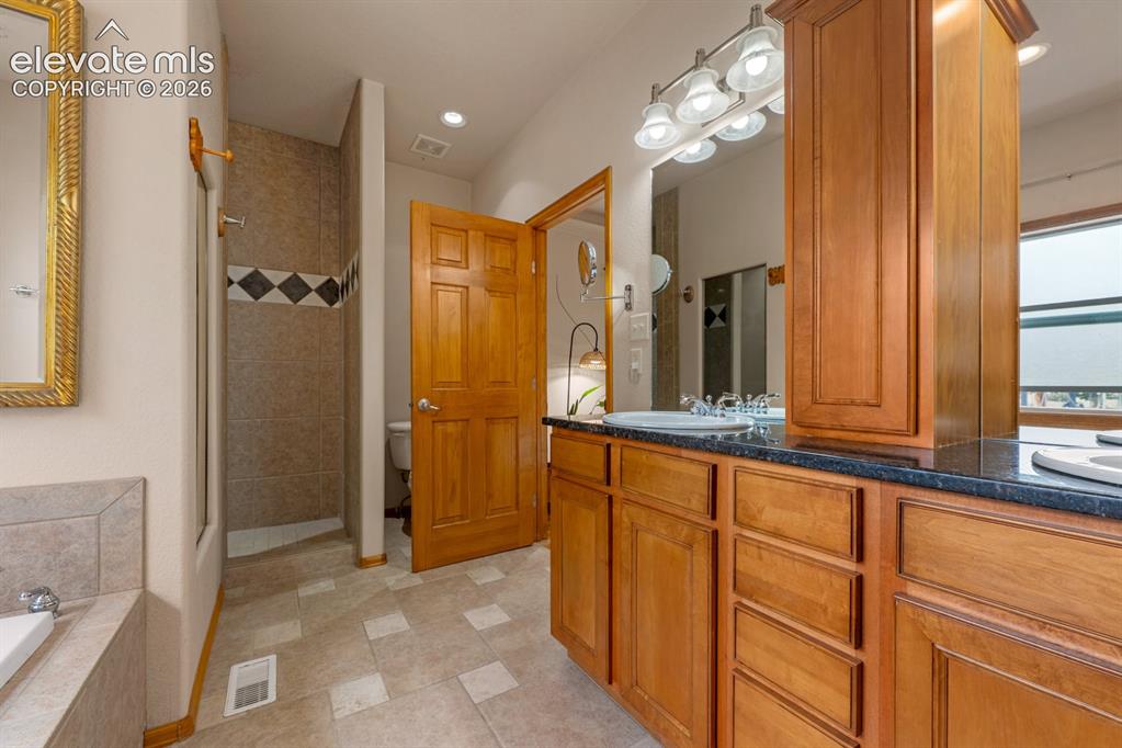 Image 23 of 50: Step into a large walk in or roll shower.  Beautiful custom tile work.