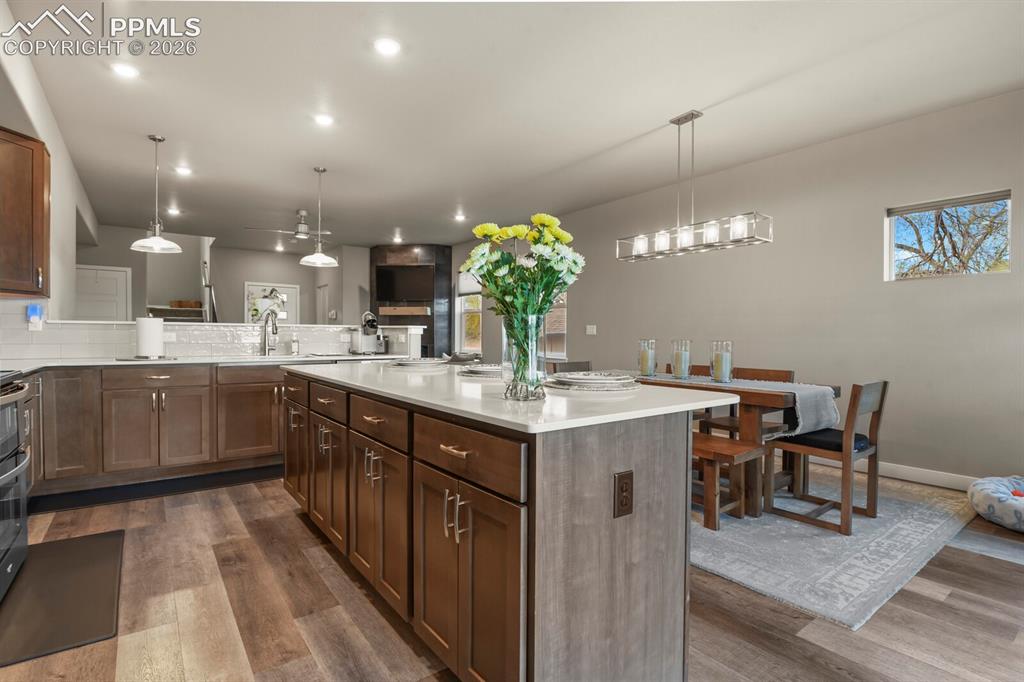 Image 12 of 33: Spacious kitchen featuring a large island with white countertops, wood-fini