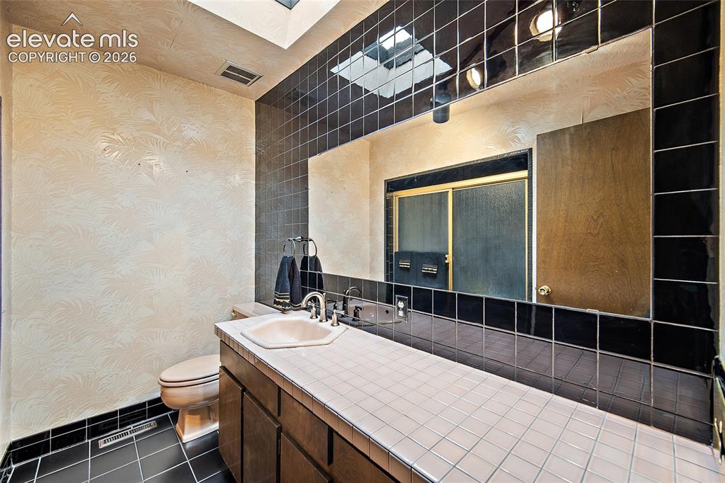 Image 22 of 50: Bathroom vanity featuring a light-colored tiled countertop with an integrat