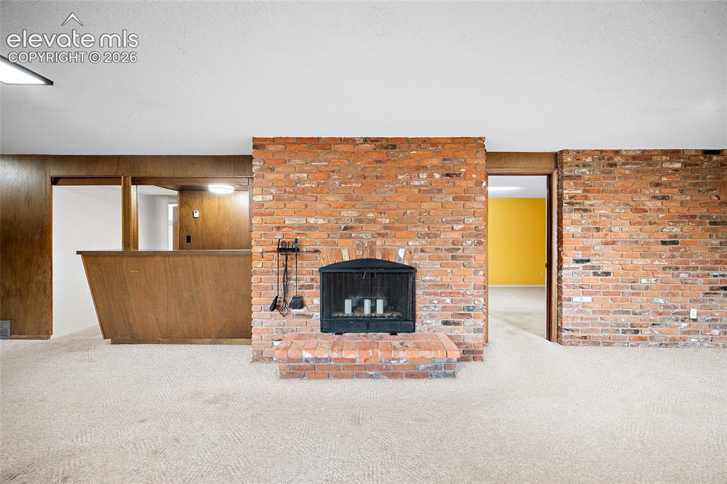 Image 27 of 50: Brick-faced fireplace with a raised hearth, flanked by a wood-paneled bar a