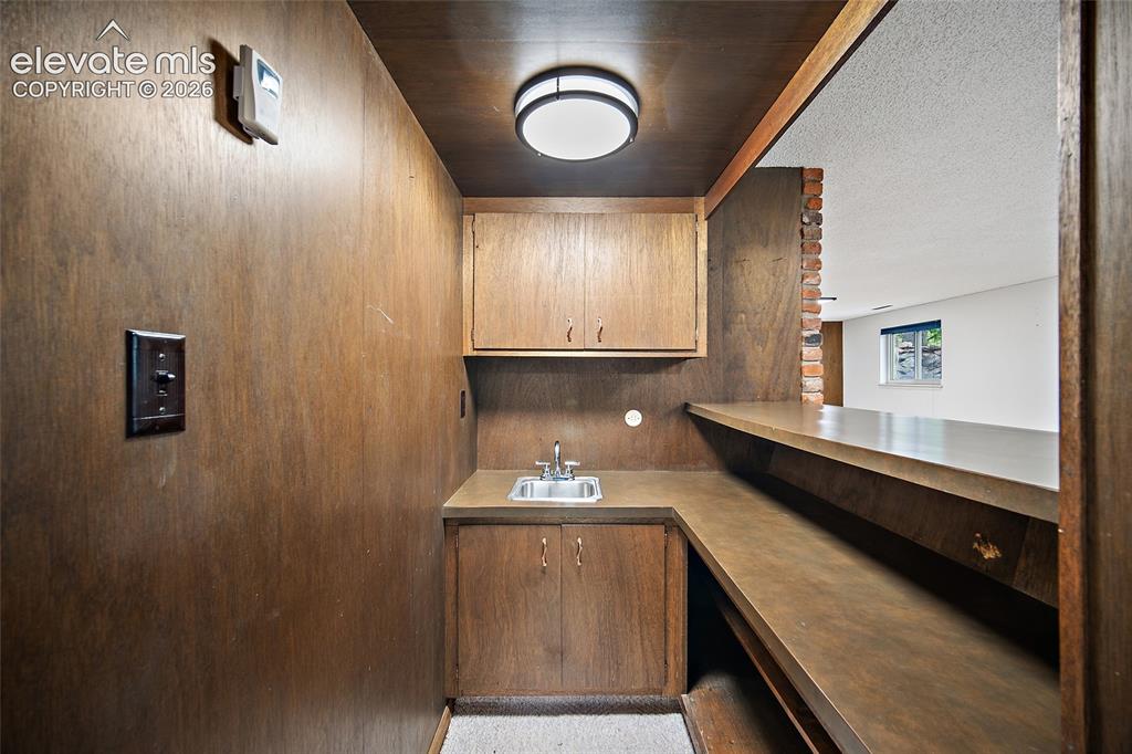 Image 29 of 50: Wet bar featuring a stainless steel sink, wood-finish cabinetry, and a buil