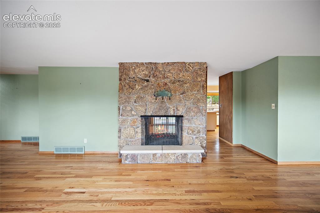 Image 3 of 50: Stone-clad fireplace with a hearth, wood-finish flooring, light green paint