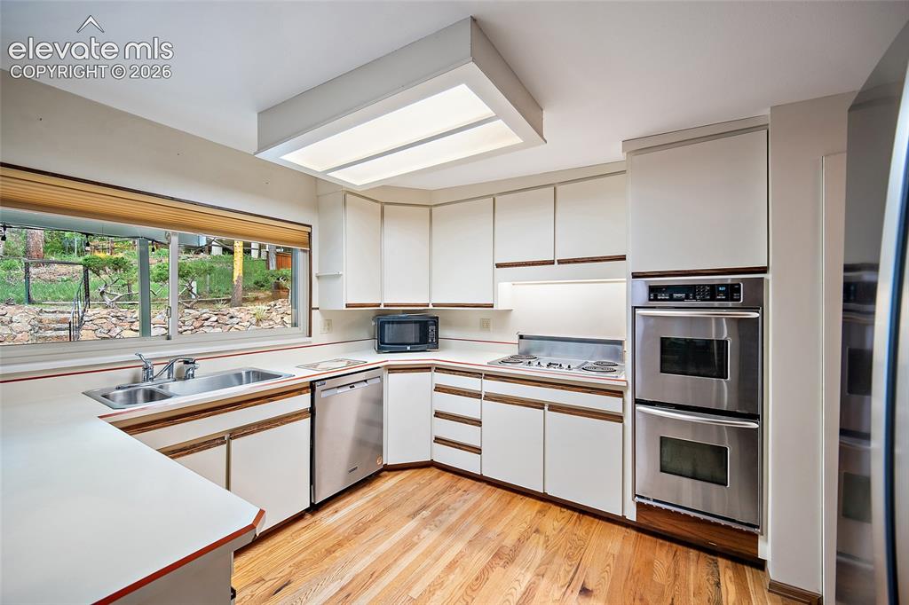 Image 6 of 50: Kitchen featuring white cabinetry with wood-finish trim, stainless steel do