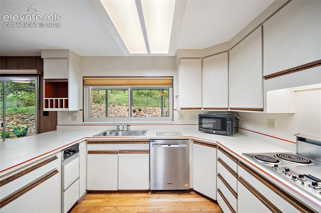Image 7 of 50: U-shaped kitchen featuring wood-finish flooring and white cabinetry with wo